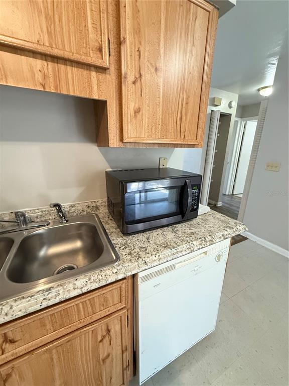 A kitchen features wood cabinets, a granite-look countertop, a stainless steel sink, and a dishwasher — 615 SW 11TH LANE UNIT D, GAINESVILLE, FL