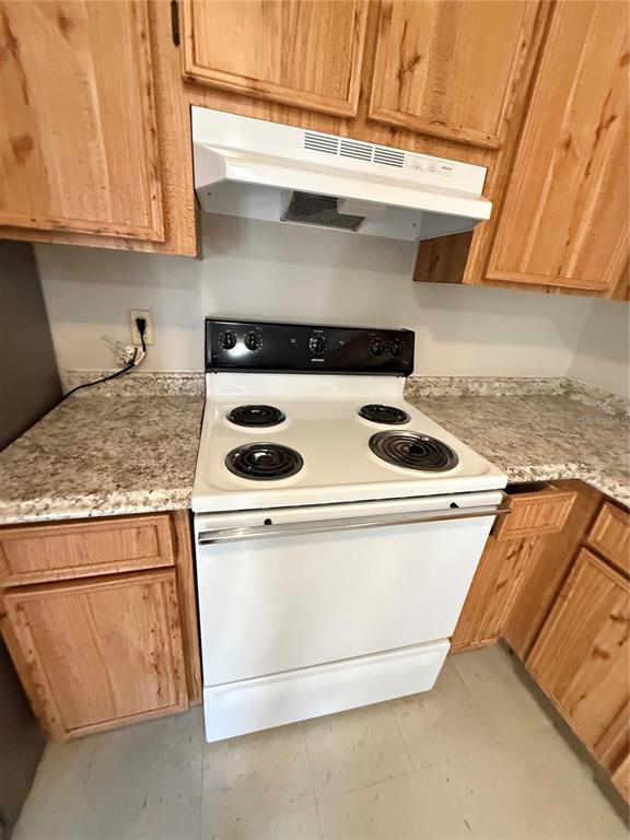 A white electric stove and range hood are positioned between wooden kitchen cabinets — 615 SW 11TH LANE UNIT D, GAINESVILLE, FL