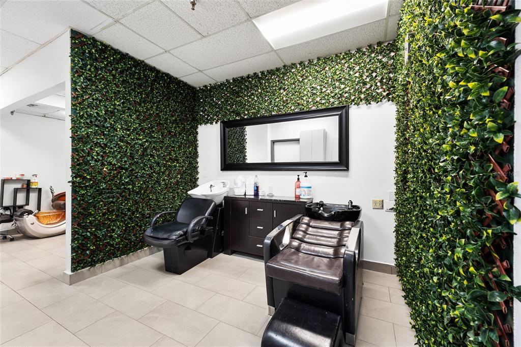A salon room features two shampoo stations, a large mirror, and walls covered in faux greenery — 4608 S JOG ROAD, GREENACRES, FL