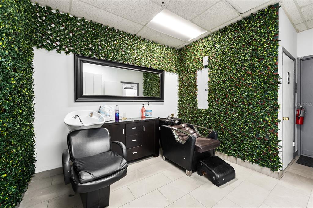 A salon room features two black chairs, a shampoo sink, and walls covered in faux greenery — 4608 S JOG ROAD, GREENACRES, FL
