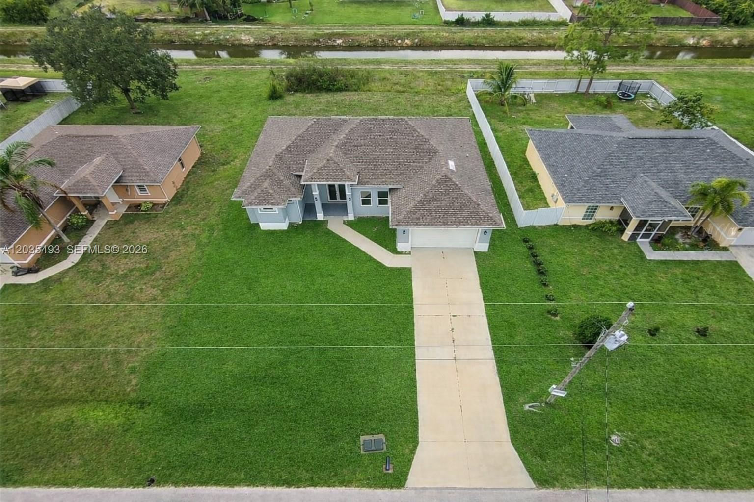 An aerial view shows a single-story house with a concrete driveway and a large lawn — 1043 albert ave # 1043, Lehigh Acres FL 33971, LEHIGH ACRES, FL