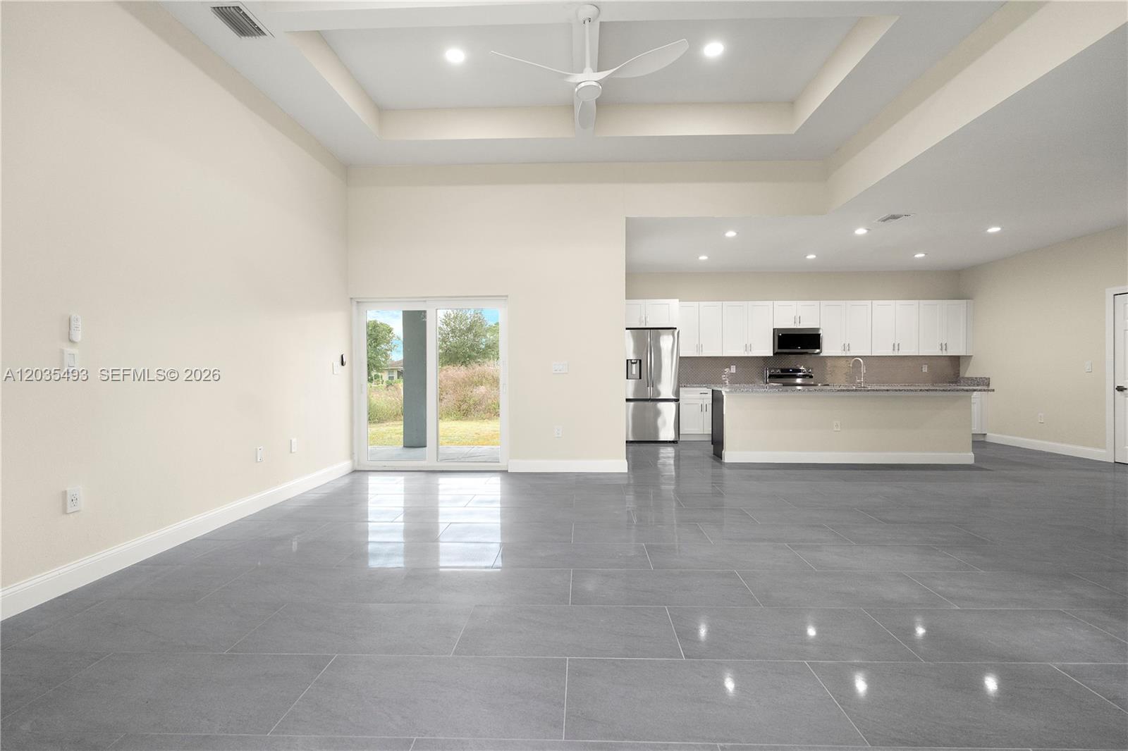 An open-concept living area features gray tile flooring, a tray ceiling, and a kitchen — 1043 albert ave # 1043, Lehigh Acres FL 33971, LEHIGH ACRES, FL