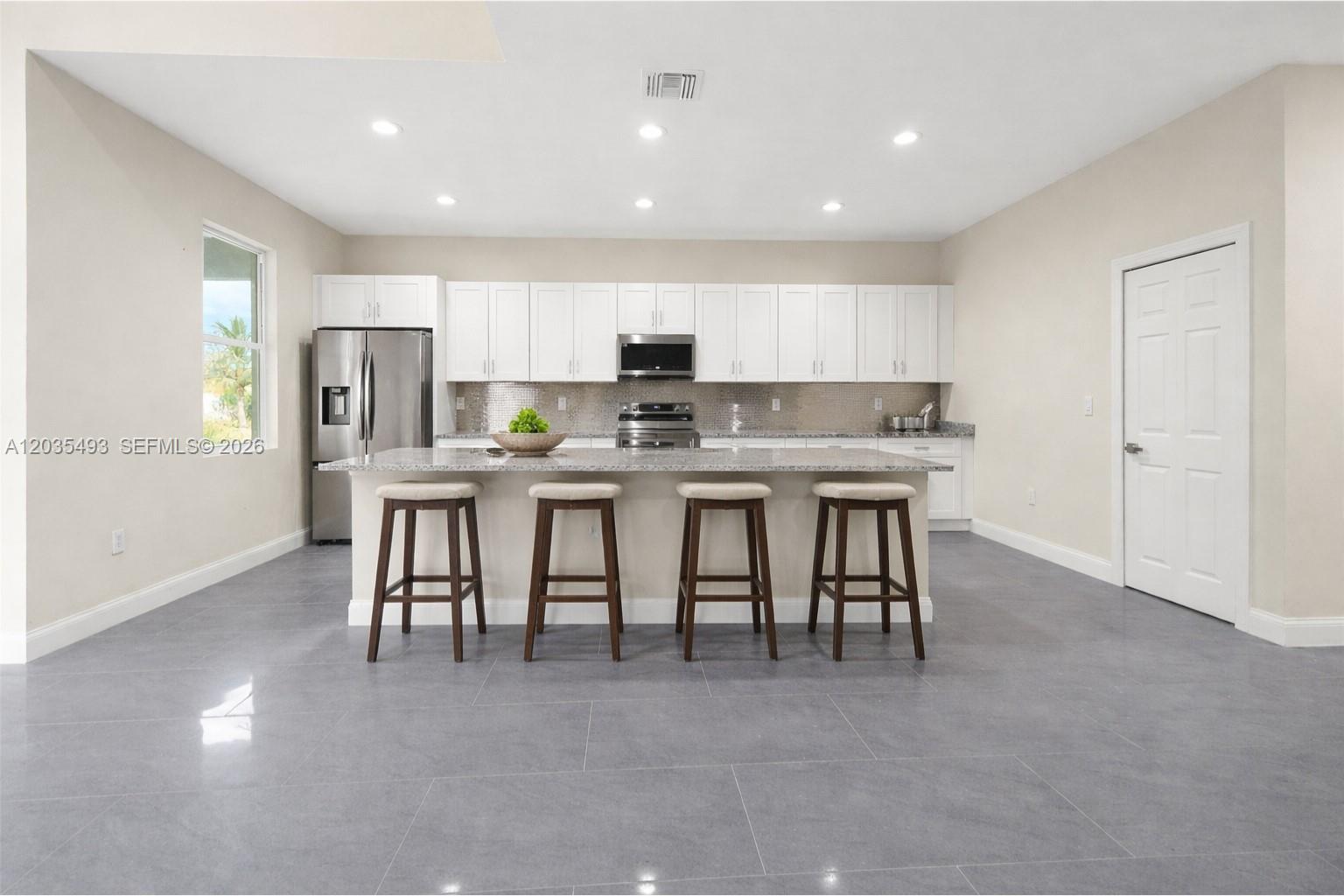 A kitchen features white cabinets, stainless steel appliances, a granite island, and gray tile flooring — 1043 albert ave # 1043, Lehigh Acres FL 33971, LEHIGH ACRES, FL