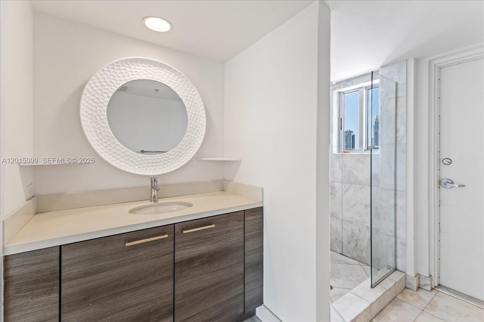 A bathroom features a wood-grain vanity, a circular textured mirror, and a glass-enclosed shower — 421 Meridian Ave # 19, Miami Beach FL 33139, MIAMI BEACH, FL