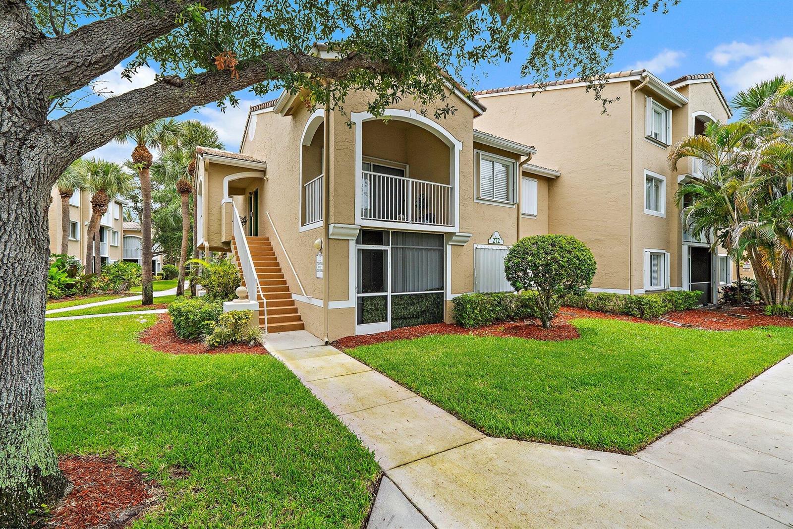 A two-story tan apartment building features a ground-floor screened patio and an upper-level balcony — 272 Village Boulevard # 7102, Tequesta FL 33469, TEQUESTA, FL