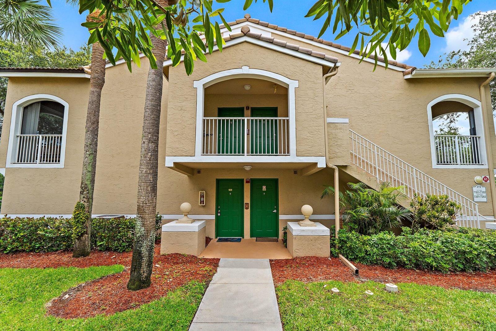 A two-story apartment building exterior features tan stucco walls, green doors, and white railings — 272 Village Boulevard # 7102, Tequesta FL 33469, TEQUESTA, FL