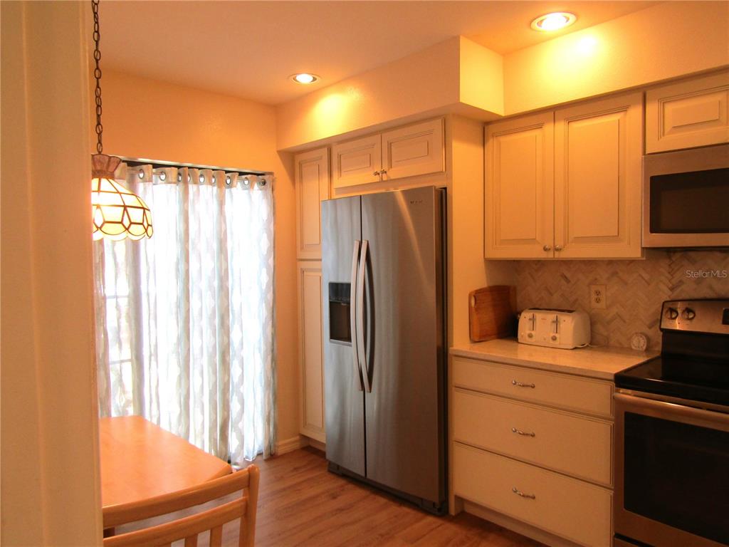 A kitchen features stainless steel appliances, light-colored cabinetry, wood-look flooring, and a dining area — 5626 PIPERS WAITE UNIT 22, SARASOTA, FL