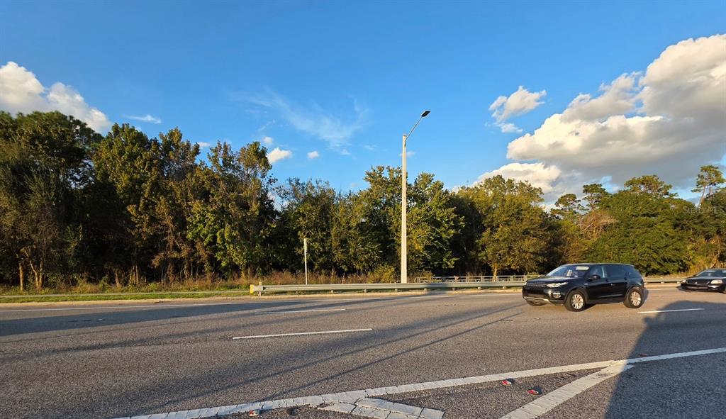 A view of a road with a black SUV driving past a wooded area — 10847 E COLONIAL DRIVE, ORLANDO, FL