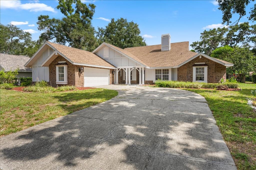 A single-story brick and white-sided house with a large driveway and a shingled roof — 136 SHEFFIELD CIRCLE E, PALM HARBOR, FL
