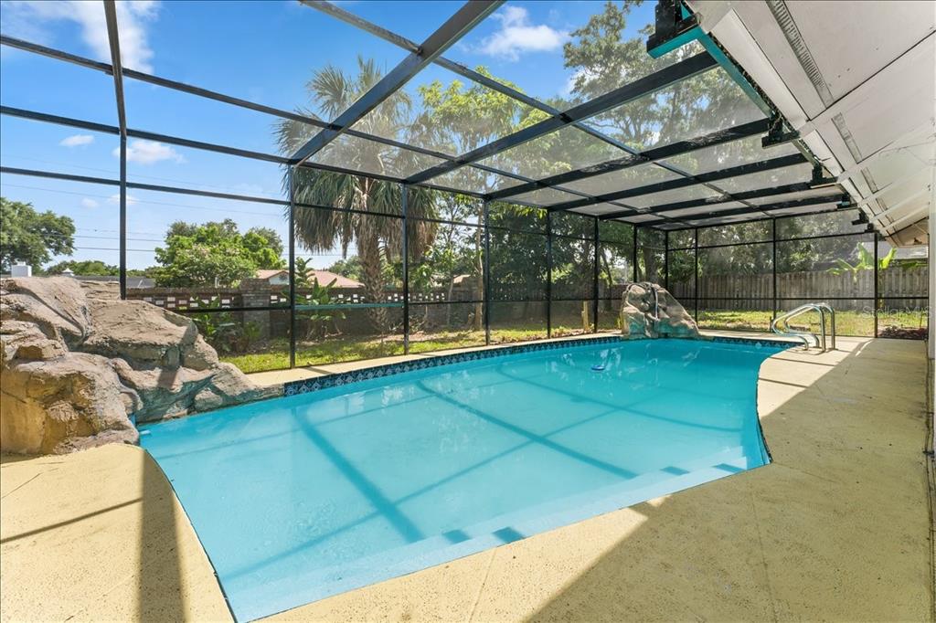 A screened-in swimming pool features a rock waterfall and a beige concrete deck — 136 SHEFFIELD CIRCLE E, PALM HARBOR, FL