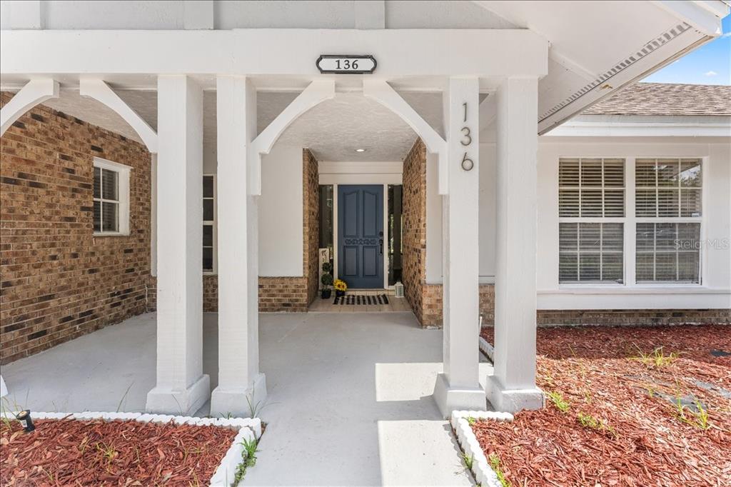 A covered front porch features white columns, brick siding, and a blue front door — 136 SHEFFIELD CIRCLE E, PALM HARBOR, FL