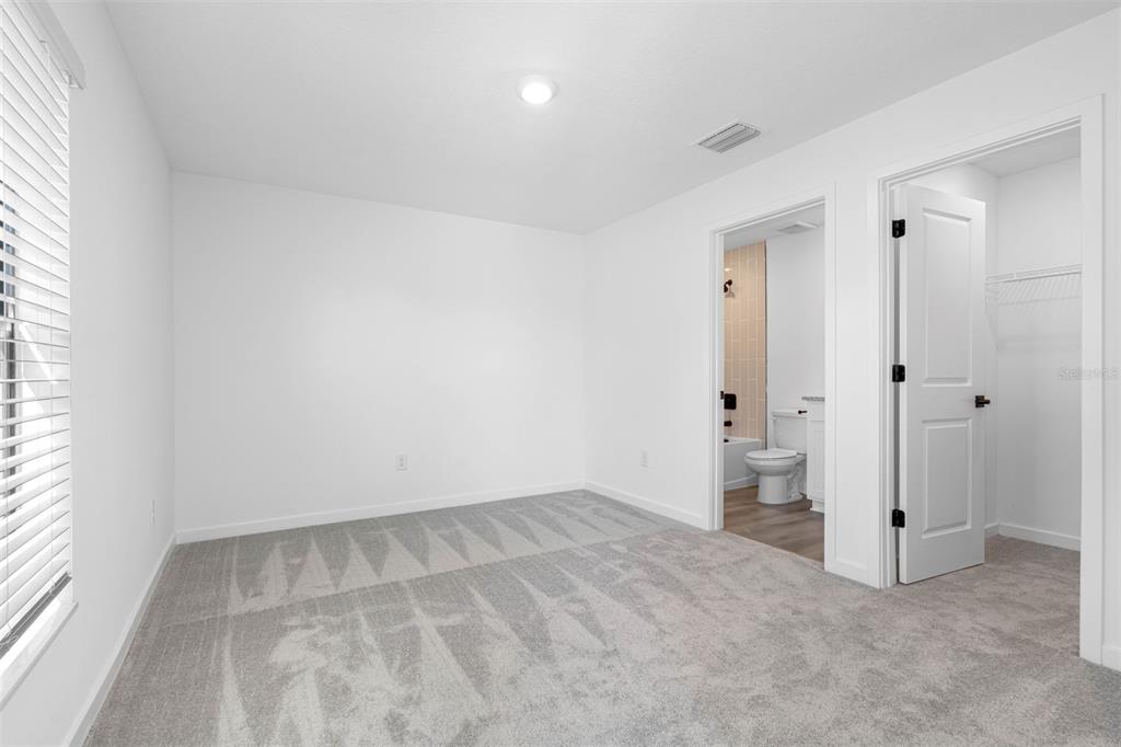 A carpeted bedroom features white walls, a window with blinds, and an attached bathroom — 13053 TRAPPER JOHN ROAD, WEEKI WACHEE, FL