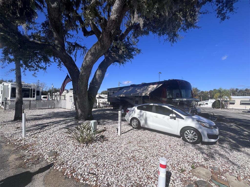 A white car is parked on a gravel lot next to a large RV and tree — 38201 MAGPIE WAY, LEESBURG, FL