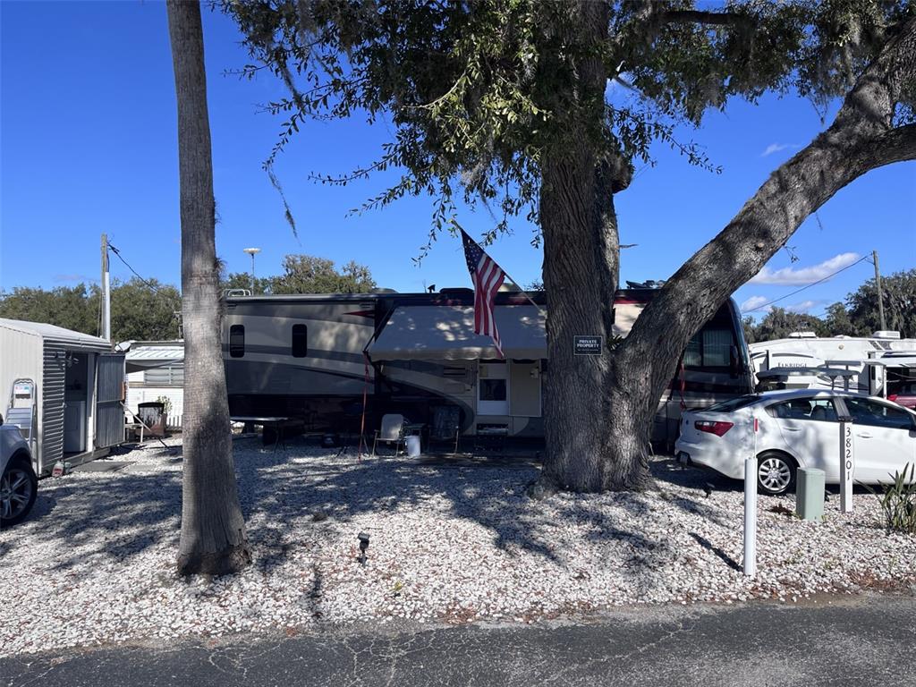 A large recreational vehicle is parked on a gravel lot beneath a large oak tree — 38201 MAGPIE WAY, LEESBURG, FL