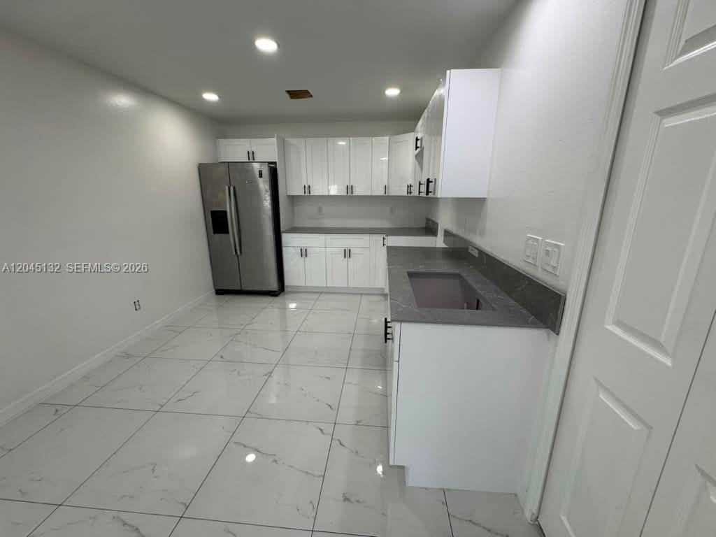 A modern kitchen features white cabinets, gray countertops, and white marble-patterned tile flooring — 732 Ichabod Ave # 732, Lehigh Acres FL 33973, LEHIGH ACRES, FL
