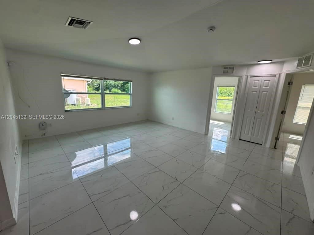 A bright, empty room features white walls, large white marble-look floor tiles, and windows — 732 Ichabod Ave # 732, Lehigh Acres FL 33973, LEHIGH ACRES, FL