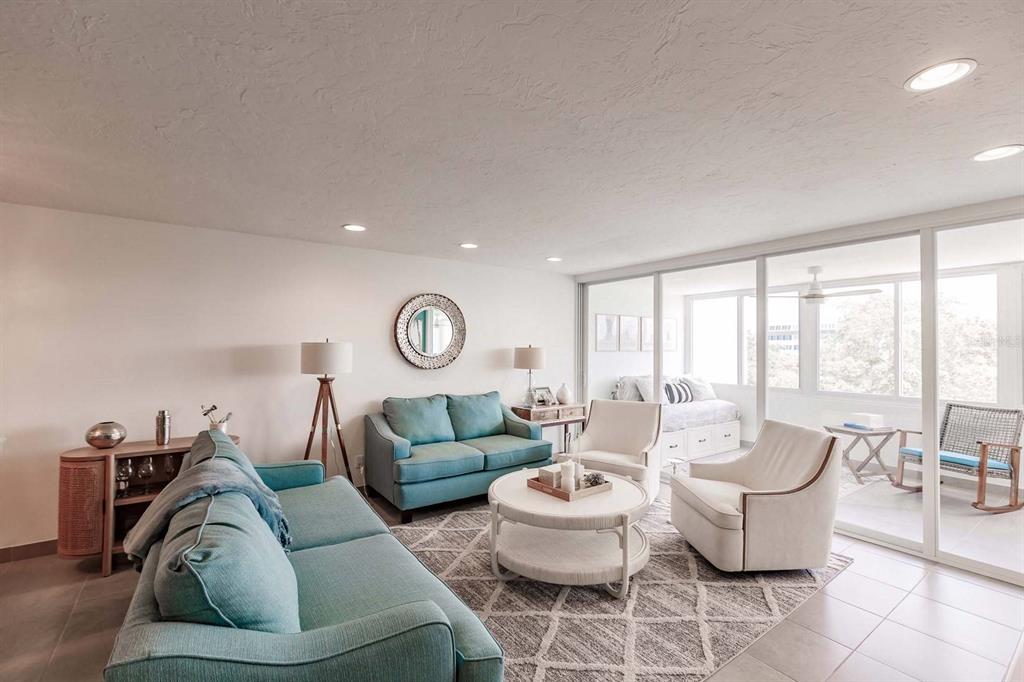 A living room features two teal sofas, two white armchairs, and a sliding glass door — 1125 W PEPPERTREE DRIVE UNIT 407, SARASOTA, FL