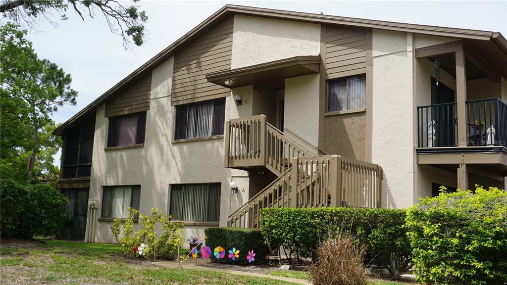 A two-story apartment building with tan stucco walls, brown trim, and an exterior wooden staircase — 12805 WEDGEWOOD WAY UNIT C, HUDSON, FL