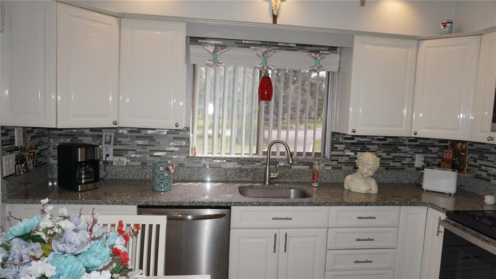 A kitchen features white cabinets, granite countertops, a stainless steel sink, and a tiled backsplash — 12805 WEDGEWOOD WAY UNIT C, HUDSON, FL