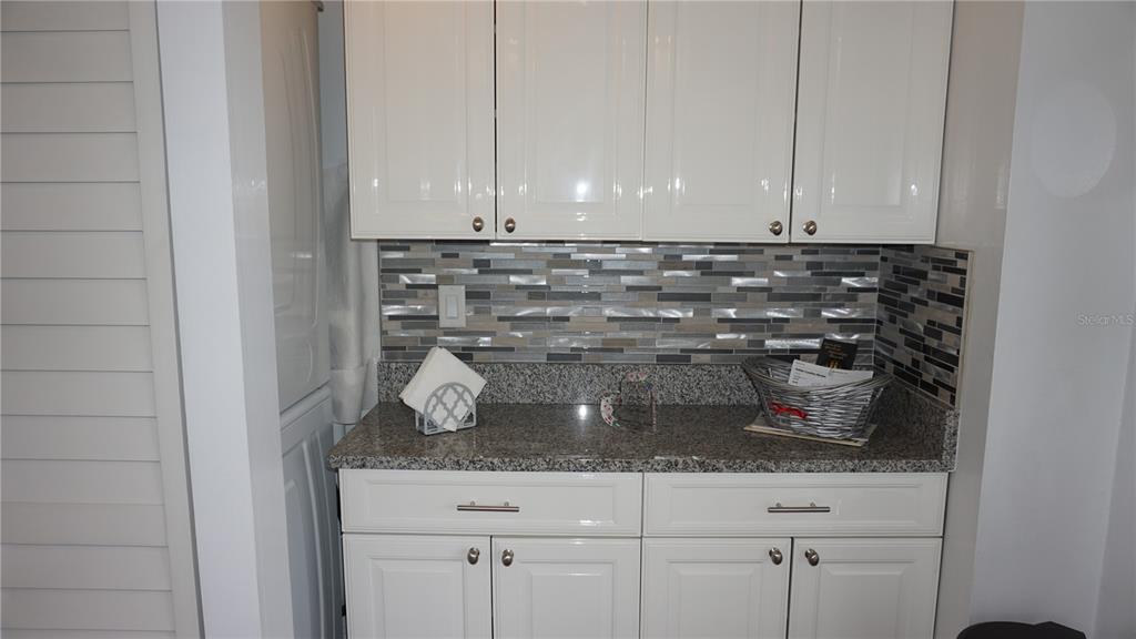 A kitchen area features white cabinets, granite countertops, and a multi-colored glass tile backsplash — 12805 WEDGEWOOD WAY UNIT C, HUDSON, FL