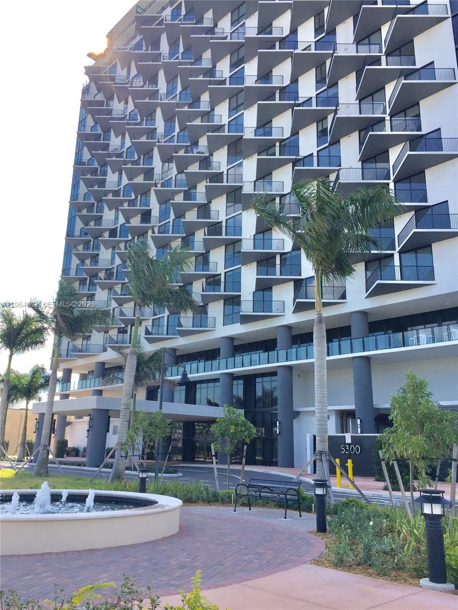 A modern high-rise building features a distinctive zigzag balcony pattern and a ground-level entrance — 5300 Paseo Blvd # 410, Doral FL 33178, DORAL, FL