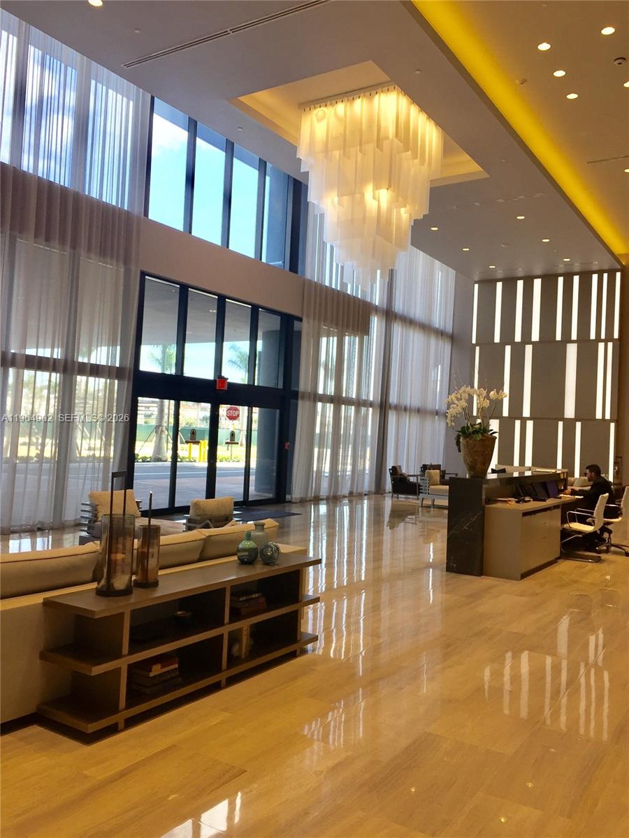 A modern building lobby features a large chandelier, floor-to-ceiling windows, and a reception desk — 5300 Paseo Blvd # 410, Doral FL 33178, DORAL, FL
