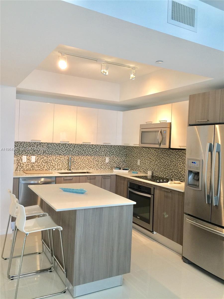 A modern kitchen features white upper cabinets, wood-grain lower cabinets, stainless steel appliances, and an island — 5300 Paseo Blvd # 410, Doral FL 33178, DORAL, FL