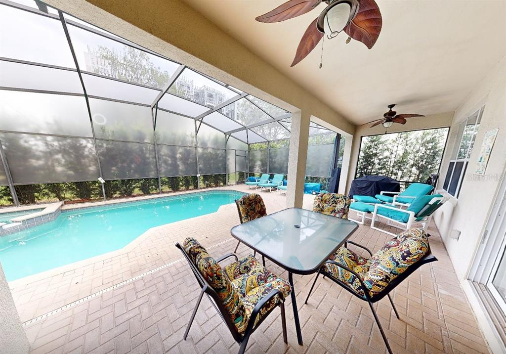 A covered patio features a dining set, ceiling fans, and a screened-in swimming pool — 2706 MANESTY LANE, KISSIMMEE, FL
