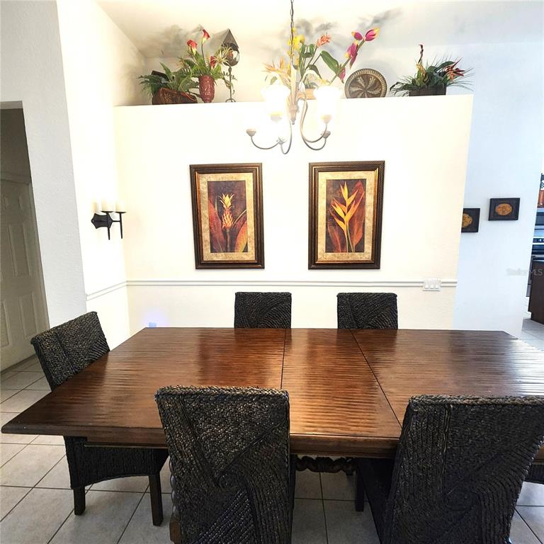 A dining room features a wooden table, woven chairs, and wall art under a chandelier — 2706 MANESTY LANE, KISSIMMEE, FL