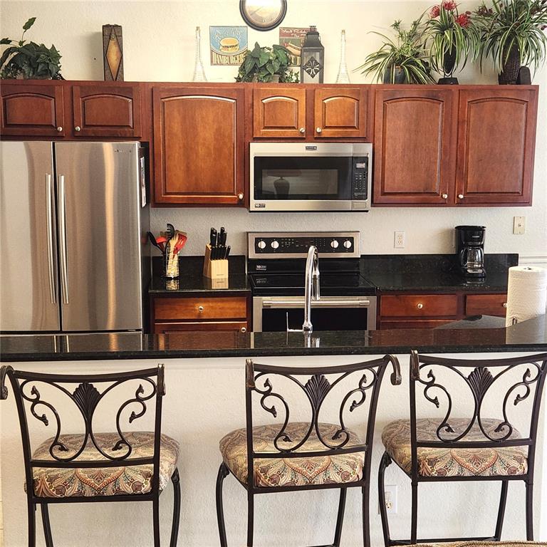 A kitchen features dark wood cabinets, stainless steel appliances, black countertops, and three bar stools — 2706 MANESTY LANE, KISSIMMEE, FL