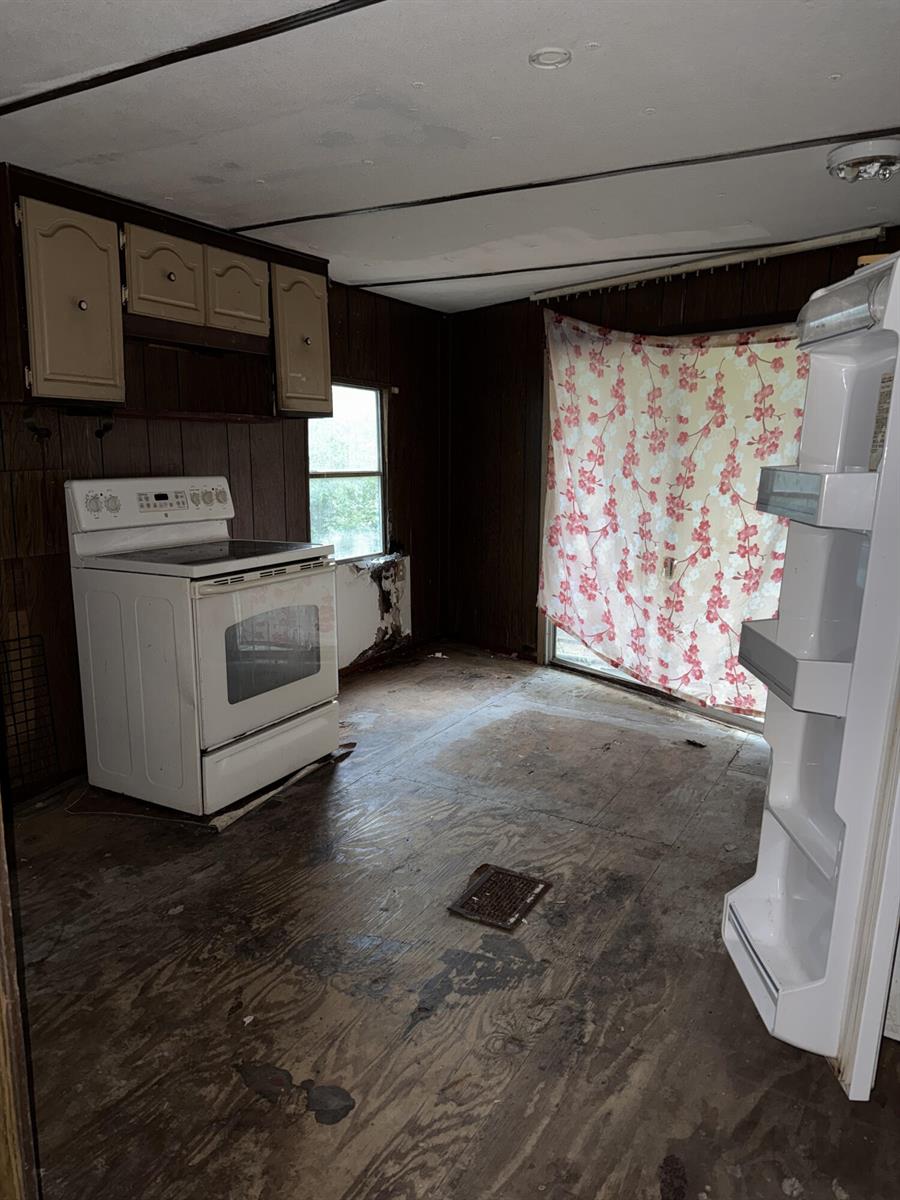 A dilapidated kitchen features dark wood paneling, a white stove, and exposed subflooring — 6072 SE 95th Trail, Okeechobee FL 34974, OKEECHOBEE, FL