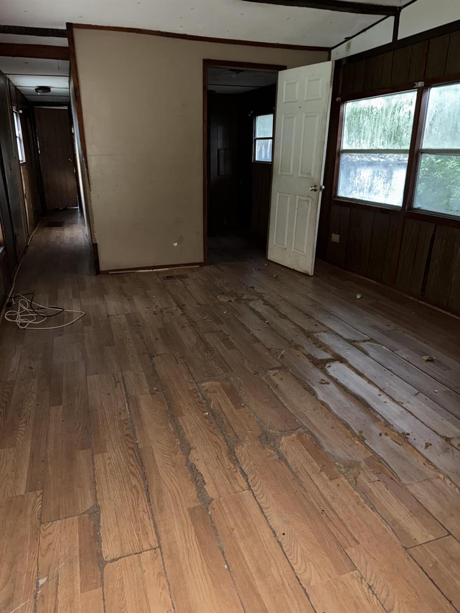 An interior view of a room with damaged wood-look flooring, wood paneling, and open doorways — 6072 SE 95th Trail, Okeechobee FL 34974, OKEECHOBEE, FL