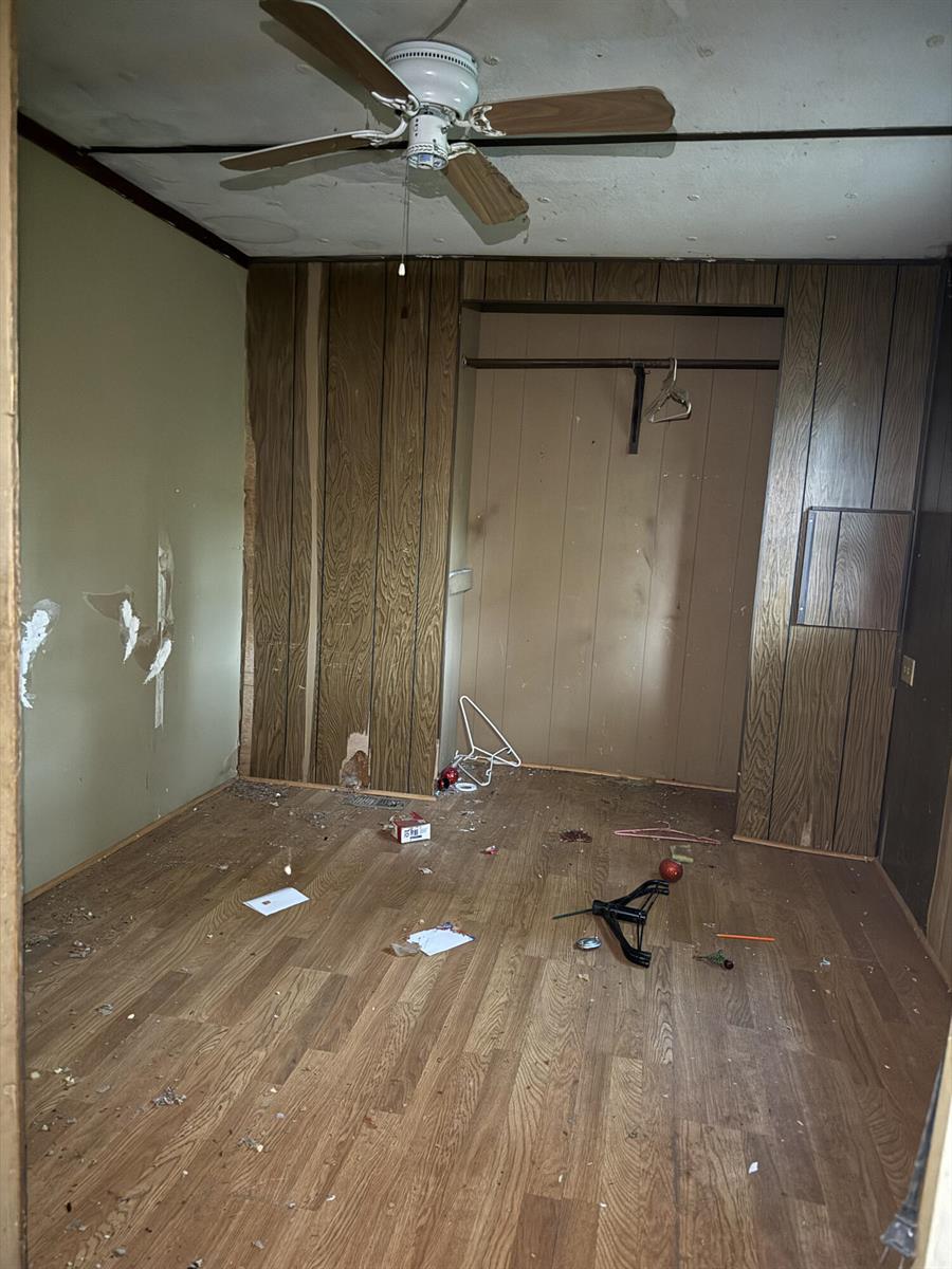 A bedroom with wood-paneled walls, a ceiling fan, and wood-look flooring in need of repair — 6072 SE 95th Trail, Okeechobee FL 34974, OKEECHOBEE, FL