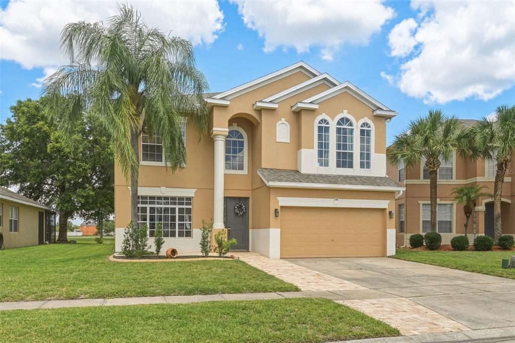 A two-story tan stucco house with a two-car garage and a paved walkway — 1518 SUN MEADOW DRIVE, ORLANDO, FL