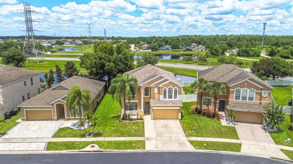 An aerial view shows three suburban houses with driveways and lawns near a pond — 1518 SUN MEADOW DRIVE, ORLANDO, FL