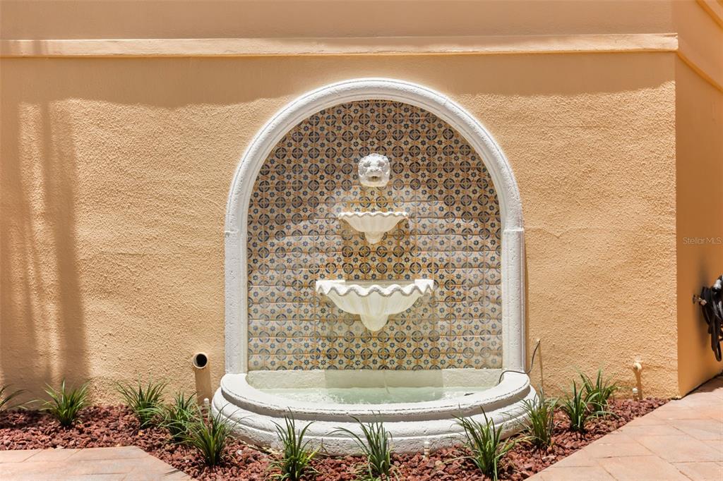 A wall-mounted tiered fountain with decorative tiles sits against a stucco exterior wall — 2480 VIA GENOVA, APOPKA, FL