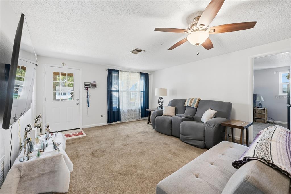 A living room features beige carpeting, a grey reclining sofa, and a ceiling fan — 2455 KIMBERLY DRIVE, DELTONA, FL