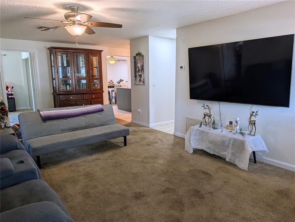 A living room features a large wall-mounted television, a grey sofa, and a wooden hutch — 2455 KIMBERLY DRIVE, DELTONA, FL