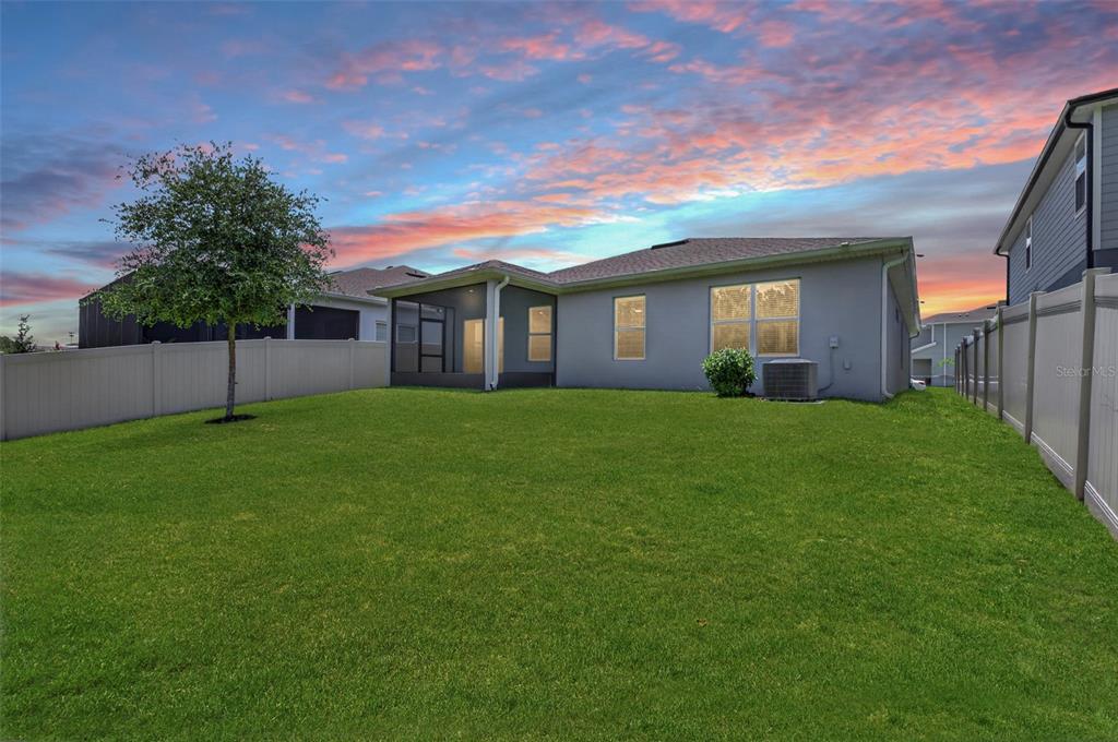 A backyard with a green lawn, a screened-in patio, and a gray house exterior — 306 EAGLE HARBOR WAY, DAYTONA BEACH, FL