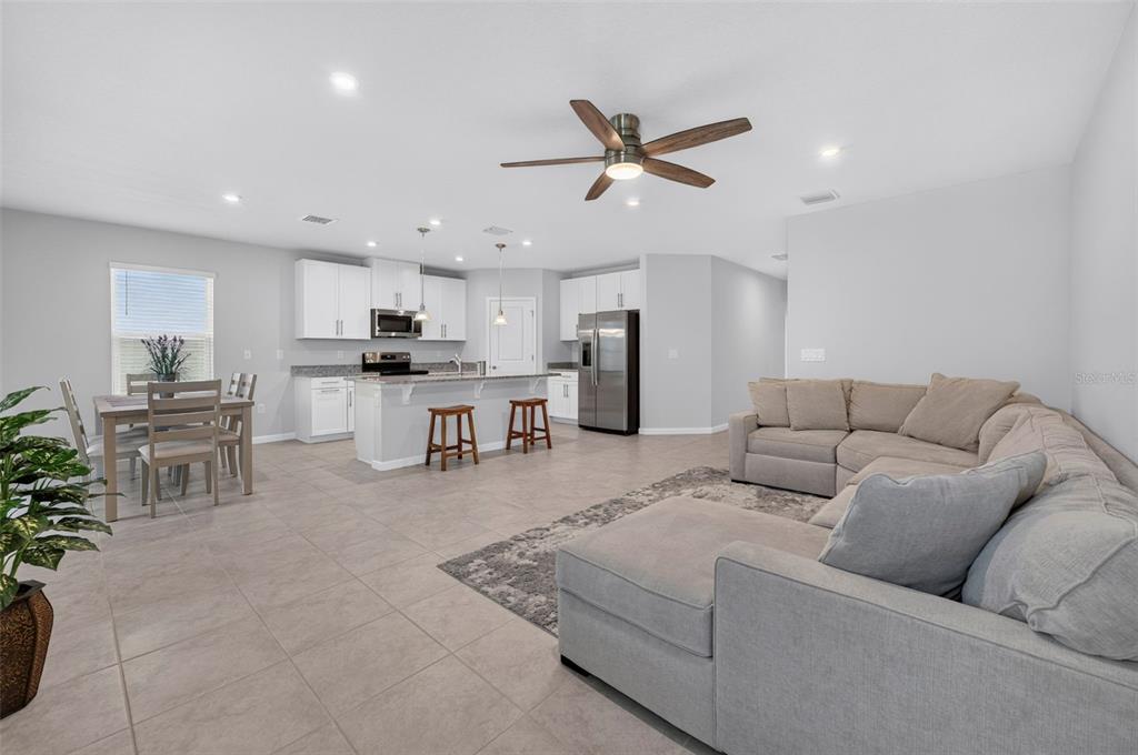 An open-concept living room and kitchen featuring light tile floors, white cabinetry, and stainless appliances — 306 EAGLE HARBOR WAY, DAYTONA BEACH, FL