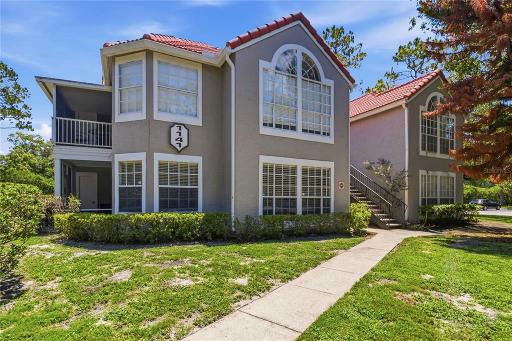 A two-story apartment building with a beige stucco exterior, red tile roof, and exterior stairs — 1141 EXCELLER CT. UNIT 105, CASSELBERRY, FL