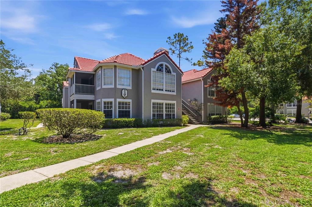 A two-story apartment building with a red tile roof and a concrete walkway outside — 1141 EXCELLER CT. UNIT 105, CASSELBERRY, FL