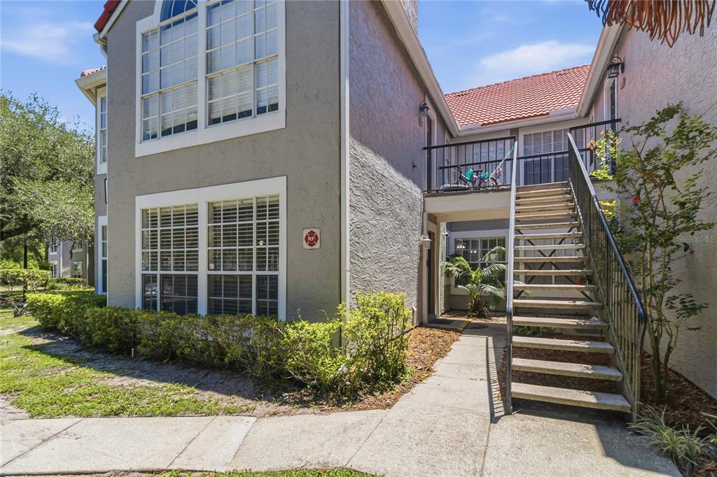 An exterior view of a two-story apartment building with a concrete staircase leading to a balcony — 1141 EXCELLER CT. UNIT 105, CASSELBERRY, FL
