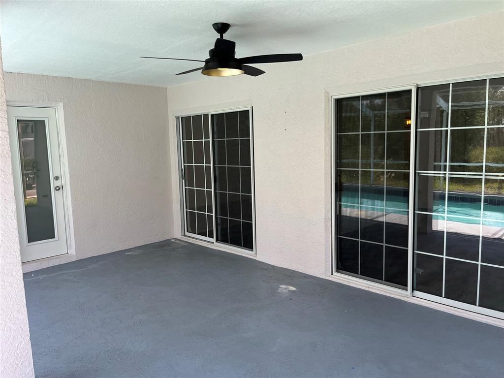 A covered patio features a ceiling fan, gray concrete flooring, and sliding glass doors — 9411 WILLOW COVE COURT, TAMPA, FL