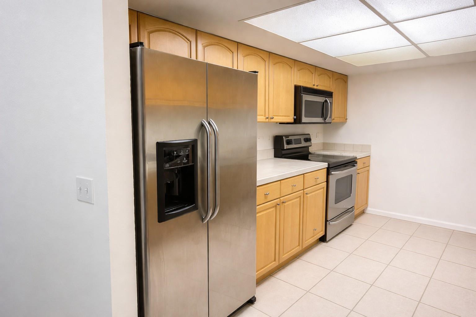 A kitchen features light wood cabinets, stainless steel appliances, white countertops, and tiled flooring — 1294 White Pine Drive # 1294, Wellington FL 33414, WELLINGTON, FL