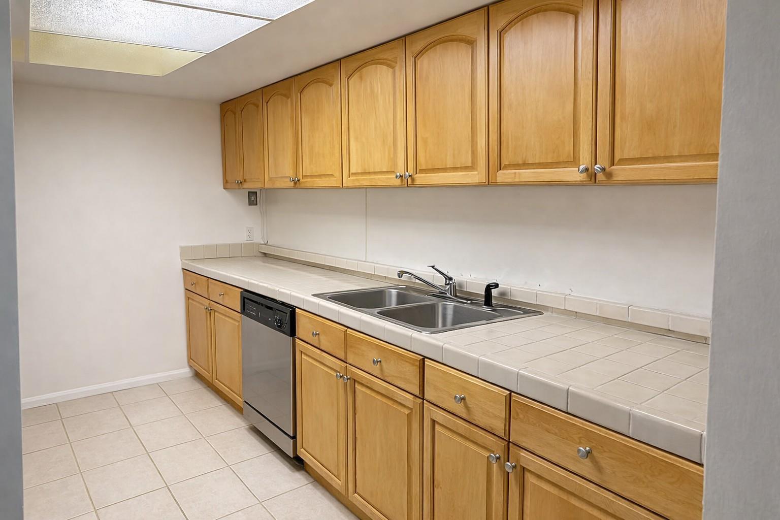 A kitchen features light wood cabinets, tiled countertops, a stainless steel dishwasher, and tile flooring — 1294 White Pine Drive # 1294, Wellington FL 33414, WELLINGTON, FL