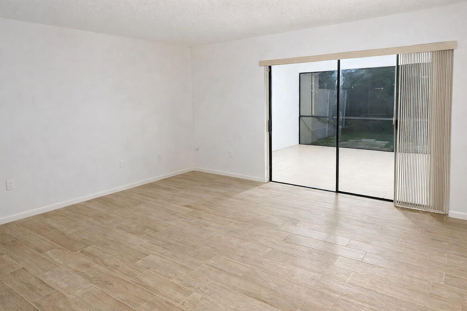 An empty room with light wood-look tile flooring and a sliding glass door to a patio — 1294 White Pine Drive # 1294, Wellington FL 33414, WELLINGTON, FL