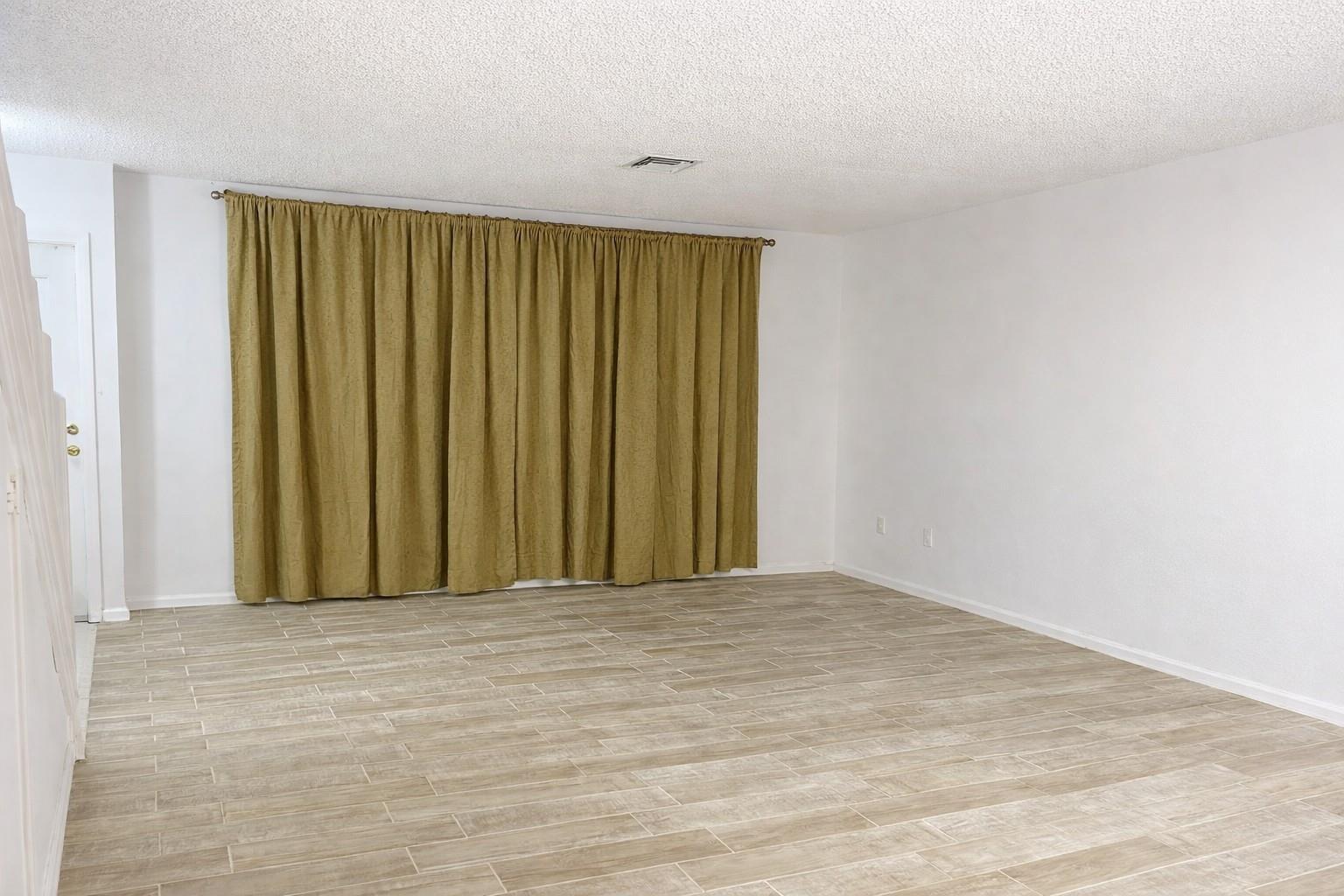 An empty room features light wood-look tile flooring, white walls, and floor-to-ceiling olive curtains — 1294 White Pine Drive # 1294, Wellington FL 33414, WELLINGTON, FL