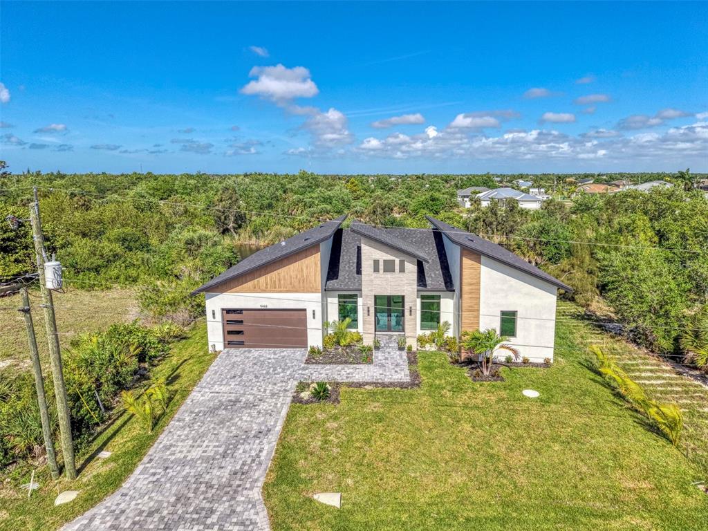 An aerial view shows a modern single-story house with a paved driveway and wood accents — 9468 ATTICA CIRCLE, PORT CHARLOTTE, FL
