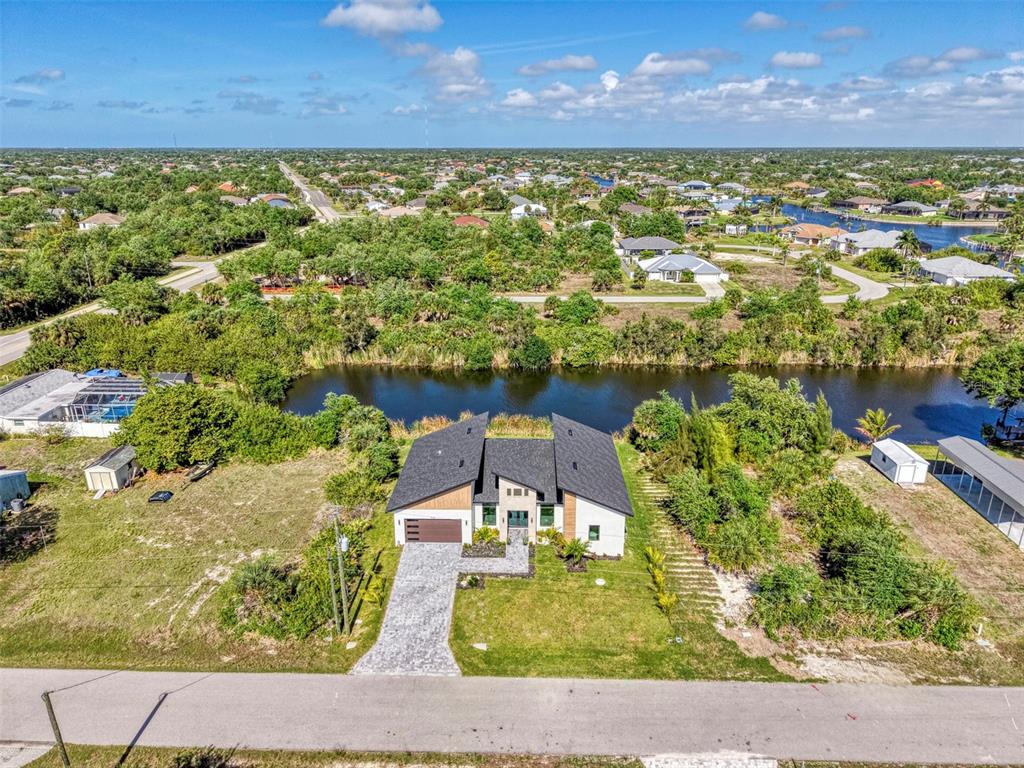 An aerial view shows a modern single-story house with a dark roof beside a canal — 9468 ATTICA CIRCLE, PORT CHARLOTTE, FL
